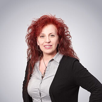 Eine Frau mit rotem Haar lächelt in die Kamera, während sie selbstbewusst in einem schwarzen Blazer posiert.