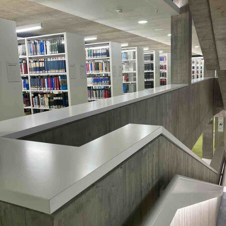 In einer modernen Bibliothek führen Treppen vorbei an gut sortierten Bücherregalen.