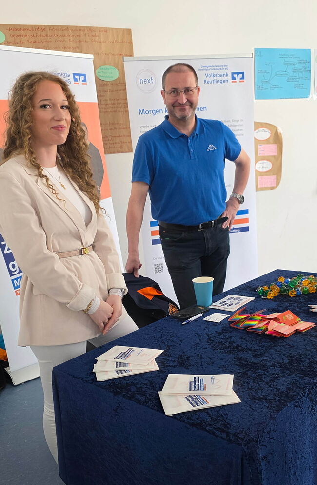 Zwei Personen stehen an einem Stand der Volksbank Reutlingen und präsentieren Informationsmaterial auf einem blauen Tisch.