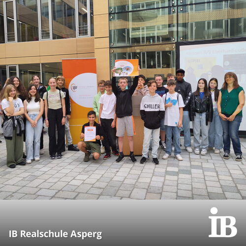 Eine Gruppe von Schülern der IB Realschule Asperg posiert stolz mit einem Preis auf einem Wettbewerb vor einem Schulgebäude.