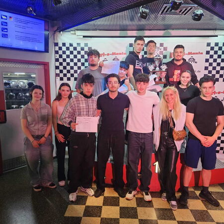 Gruppe von Menschen bei einer Preisverleihung in einer Kartbahn, lächelnd und stolz mit Trophäen in der Hand. | © Name
