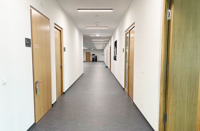 Ein heller Flur im Neubau zeigt mehrere Bürotüren und eine moderne, minimalistische Gestaltung.