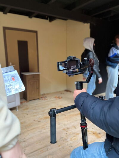 Eine Person filmt in einem Raum mit einem Stabilisator, während andere im Hintergrund vorbeigehen.