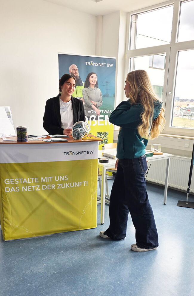 Eine Mitarbeiterin von Transnet BW berät eine junge Frau am Informationsstand über das Netz der Zukunft.