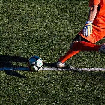 Ein Fußballspieler in orangener Ausrüstung tritt den Ball während eines Turniers auf einem grünen Spielfeld.
