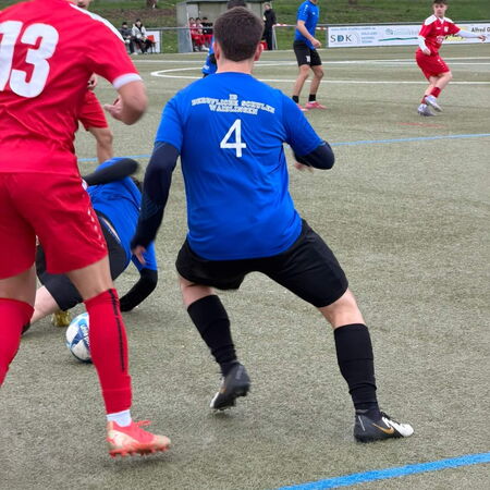 Ein Fußballspieler in blauer Trikots kämpft um den Ball, während ein Gegner in Rot ihn herausfordert.