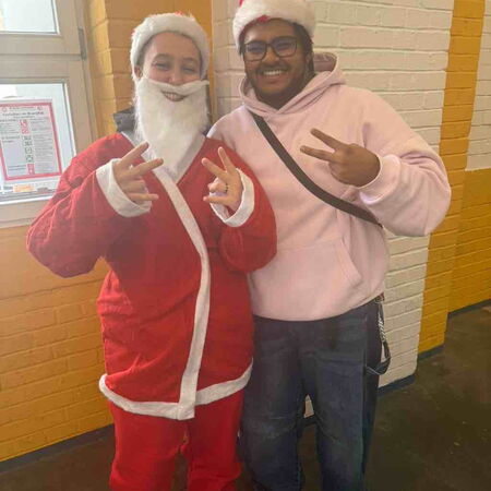 Zwei Personen in Weihnachtsmützen posieren fröhlich für ein Bild, wobei eine als Weihnachtsmann verkleidet ist.