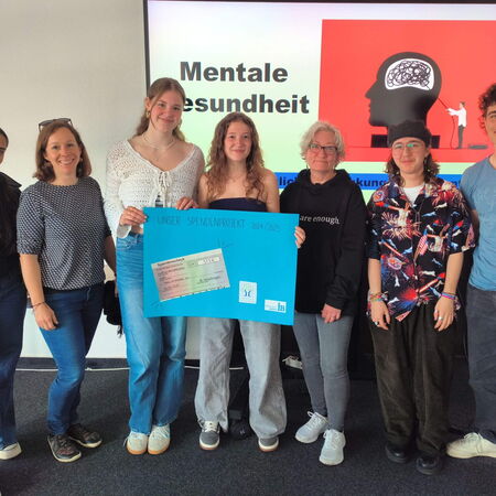 Eine Gruppe von sieben Personen präsentiert ein Plakat für ein Spendenprojekt zur Förderung der mentalen Gesundheit.