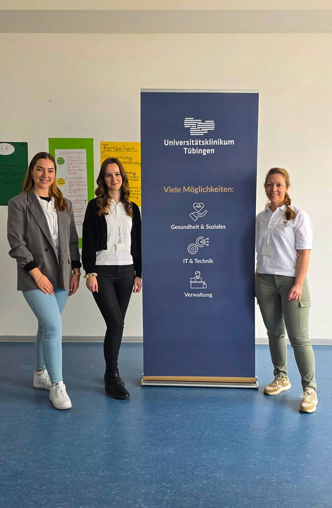 Drei Frauen stehen stolz vor einem Banner des Universitätsklinikums Tübingen mit Informationen zu Karrieremöglichkeiten.