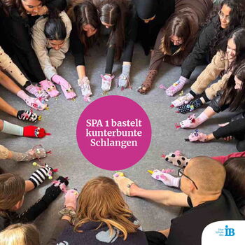 Eine Gruppe von Menschen bastelt bunte Schlangen aus Socken und zeigt sie in einem Kreis.