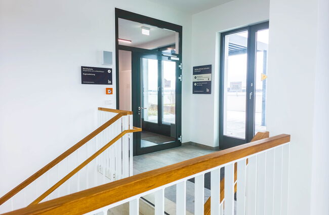 Der Eingang zum 4. Obergeschoss zeigt eine moderne Treppe und große Glastüren, die Licht hereinlassen.