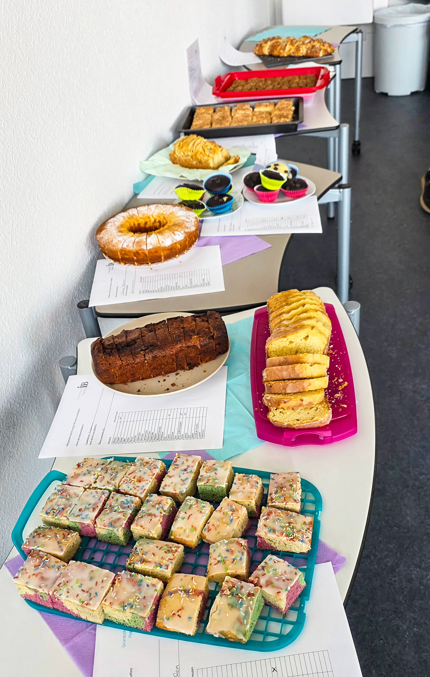 Auf einem Tisch sind verschiedene Kuchen und Snacks aus einer Grundschule zum Tag der offenen Tür angerichtet.