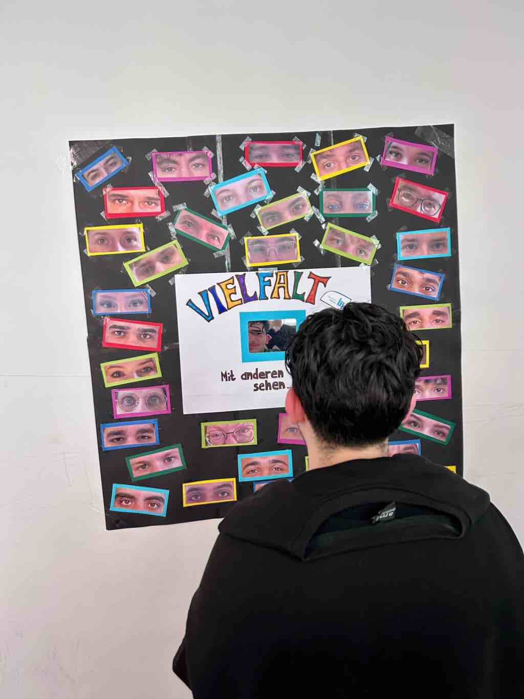 Eine Person betrachtet ein Plakat mit dem Titel "Vielfalt" und vielen bunten Augenbildern. | © Name