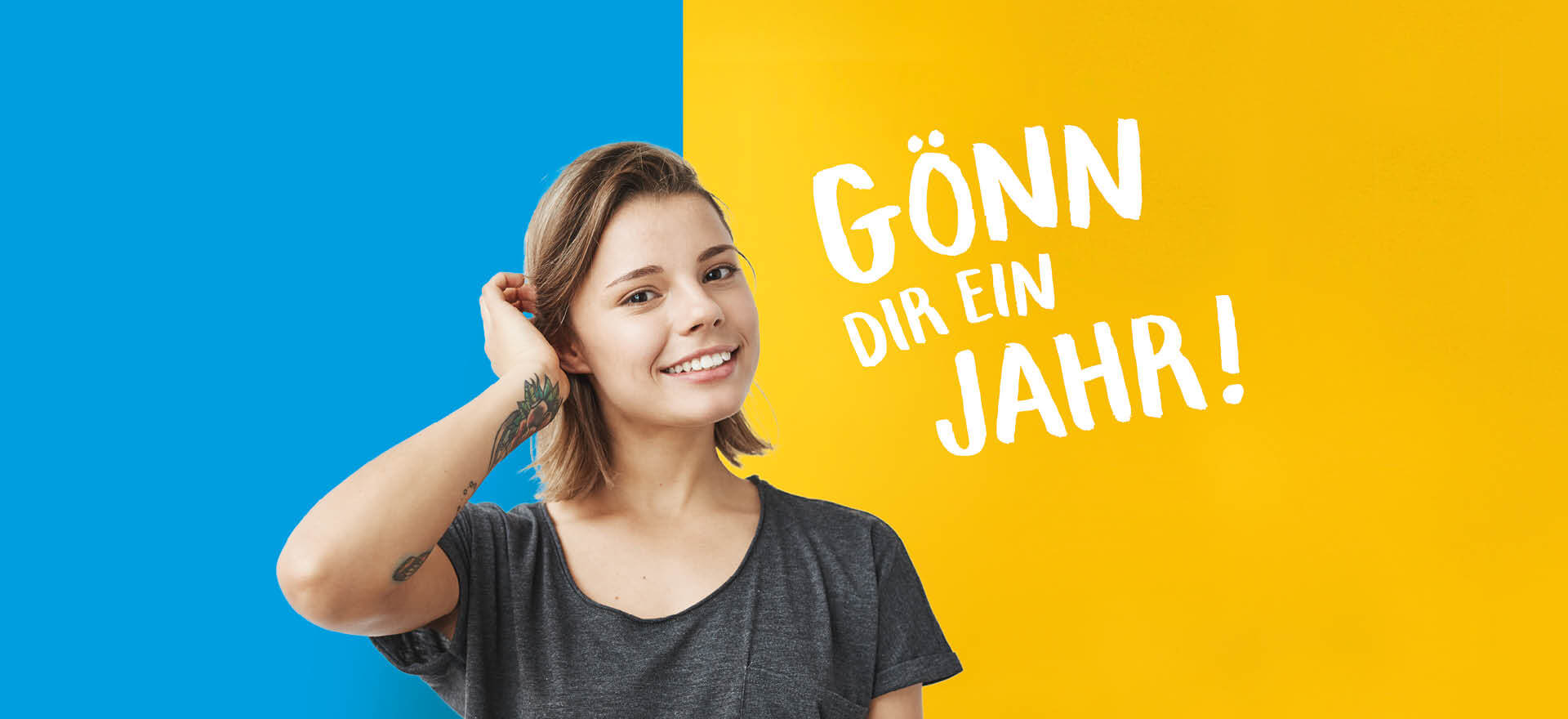 Eine lächelnde junge Frau steht vor einem zweifarbigen Hintergrund mit dem Text "Gönn dir ein Jahr!" auf der rechten Seite.