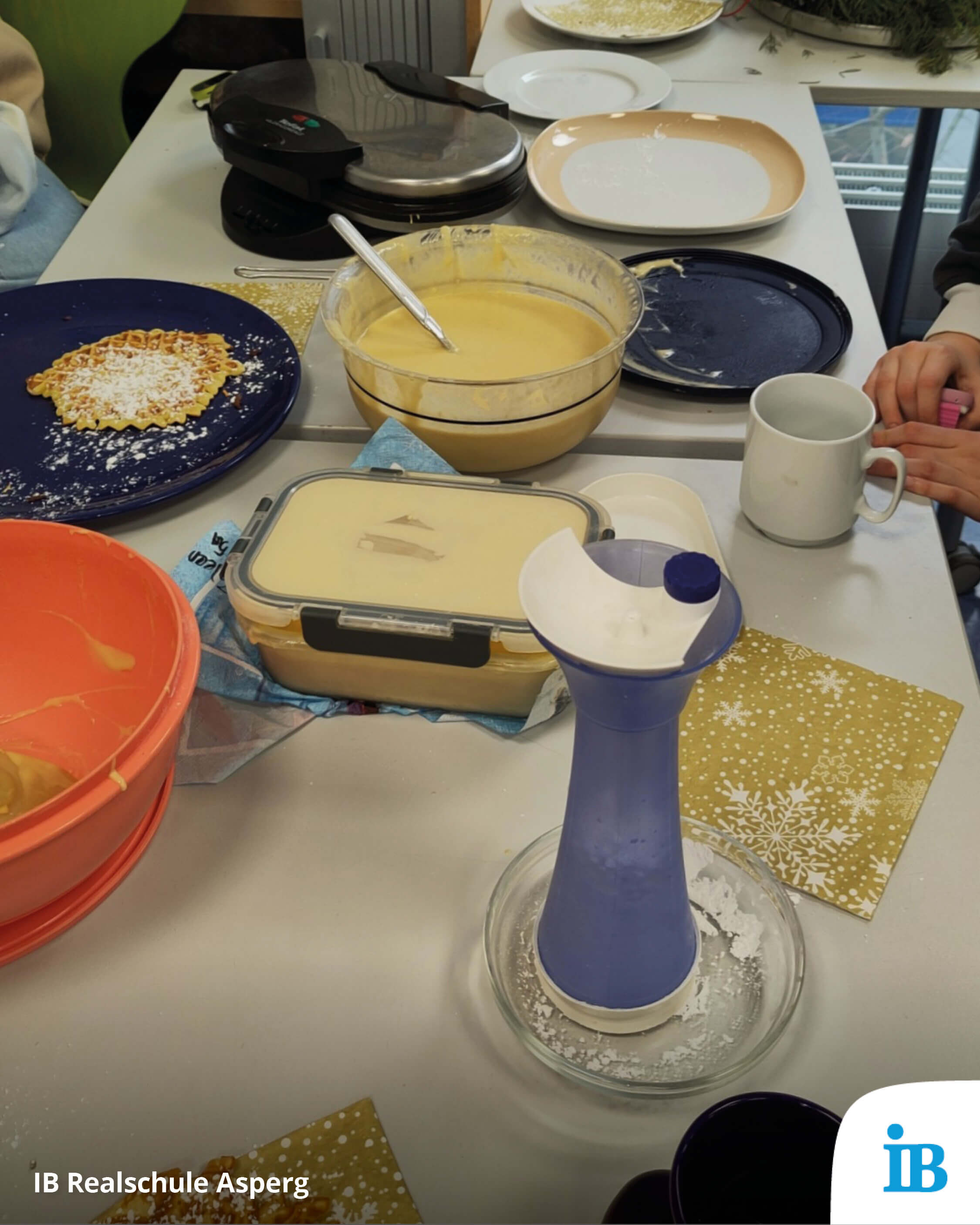 Ein Tisch ist gedeckt mit Waffeleisen, Teig und einer frisch gebackenen Waffel für einen Adventsnachmittag.
