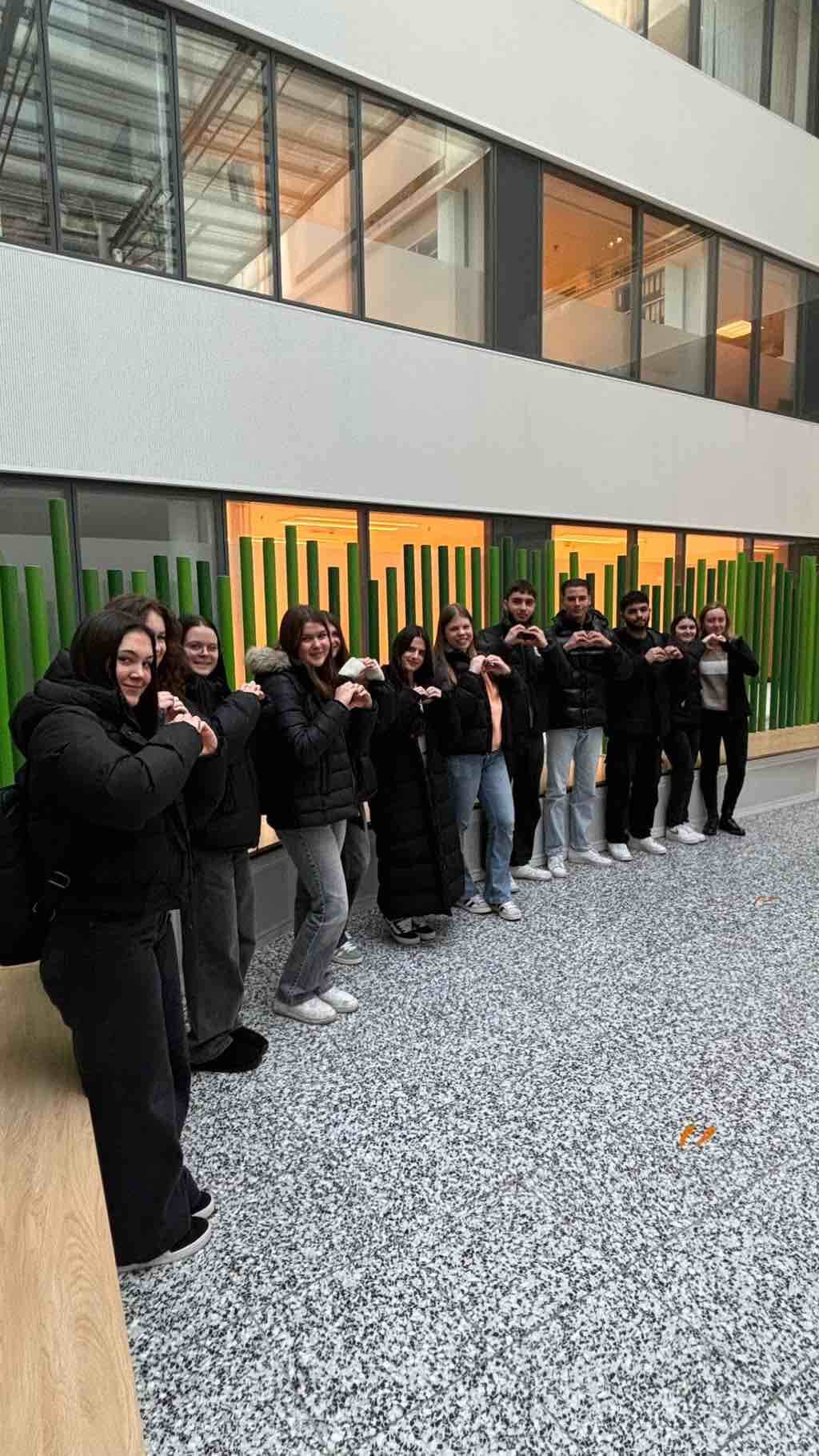 Eine Gruppe junger Menschen steht in einem modernen Gebäude und formt mit den Händen Herzgesten.