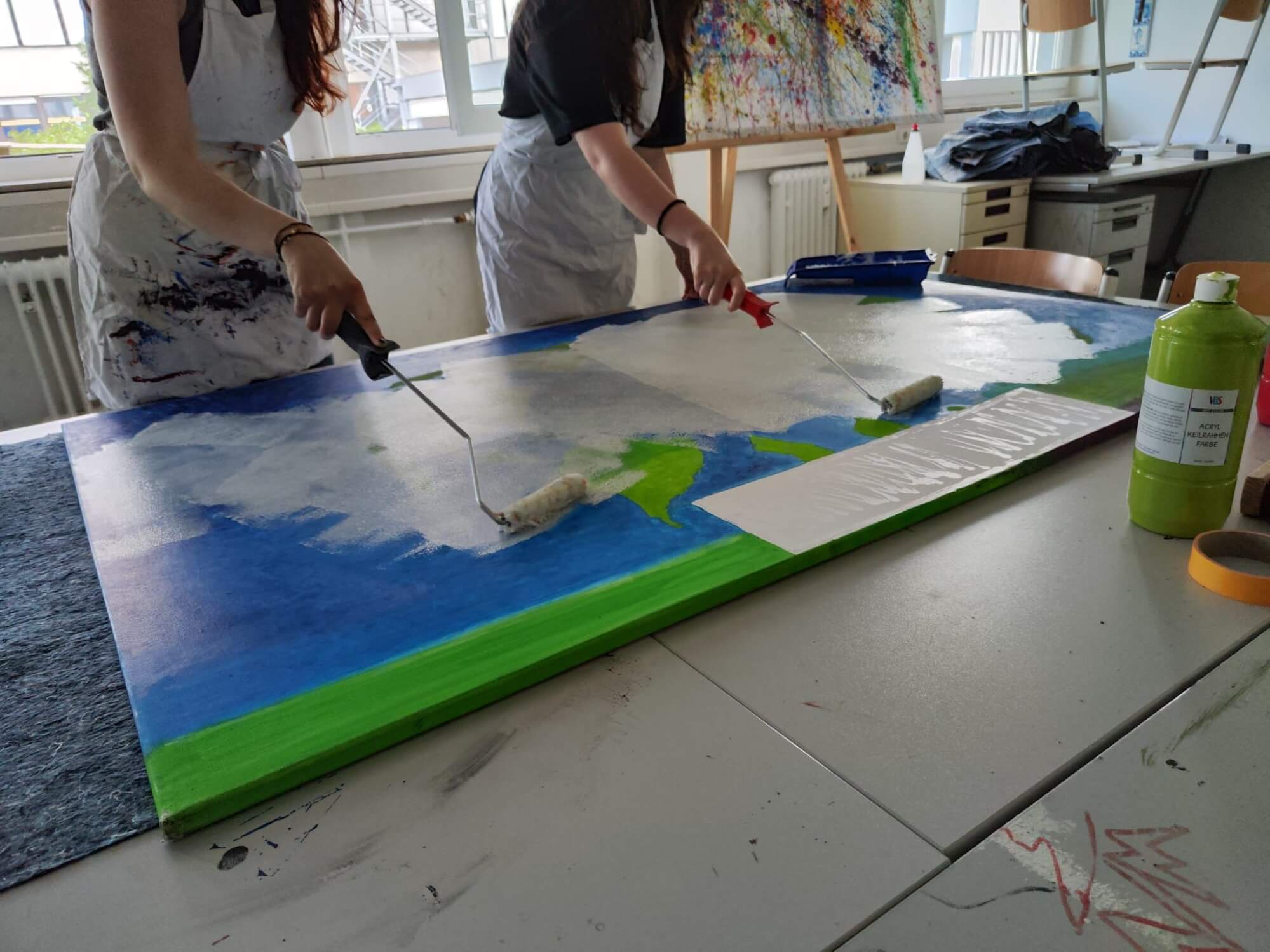Zwei Personen bemalen eine große Leinwand mit Farbrollen, um ein kreatives Kunstprojekt im Atelier zu gestalten.