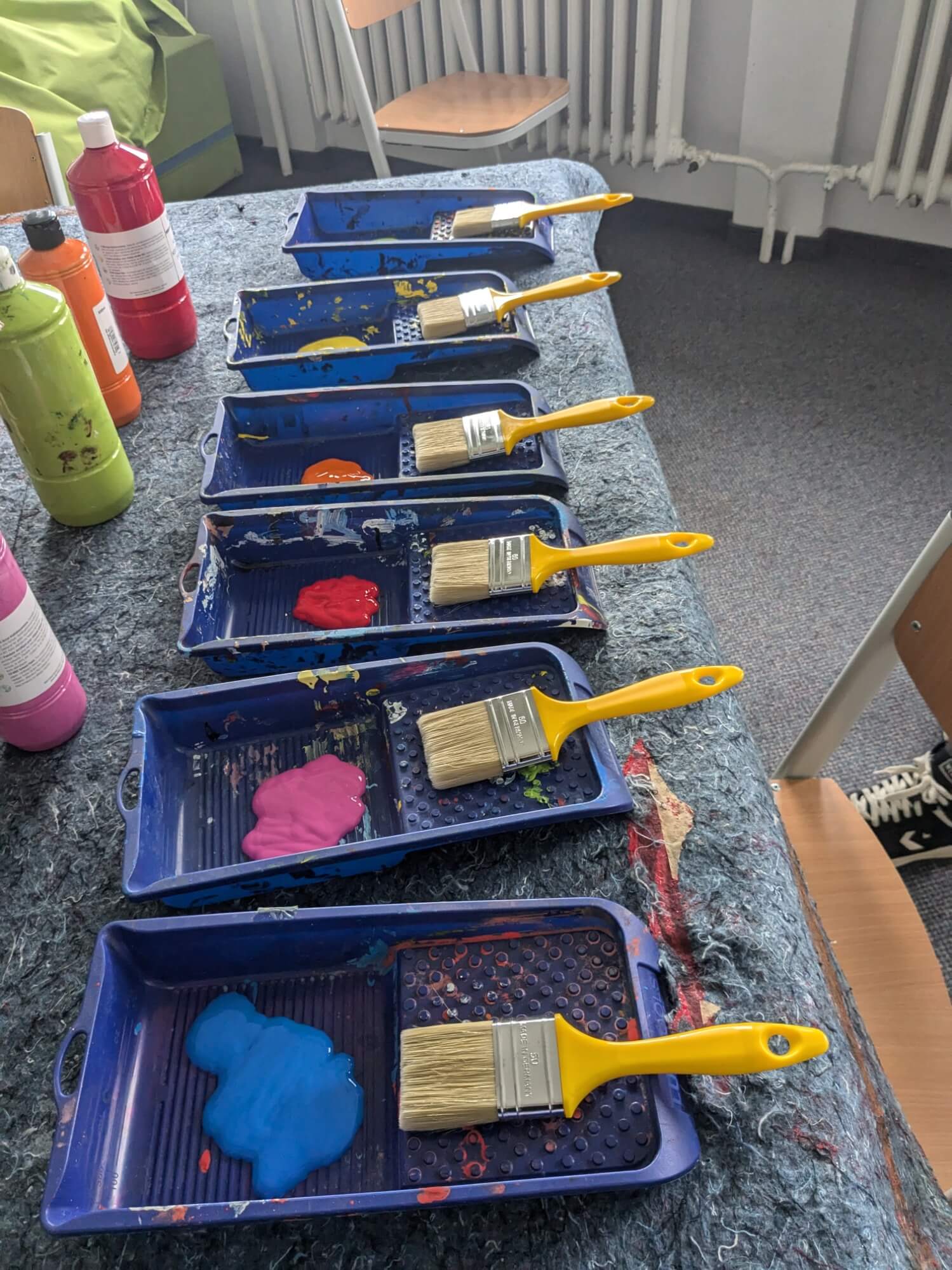 Gelbe Pinsel liegen auf blauen Farbpaletten, gefüllt mit bunten Farben, und warten auf kreatives Malen.